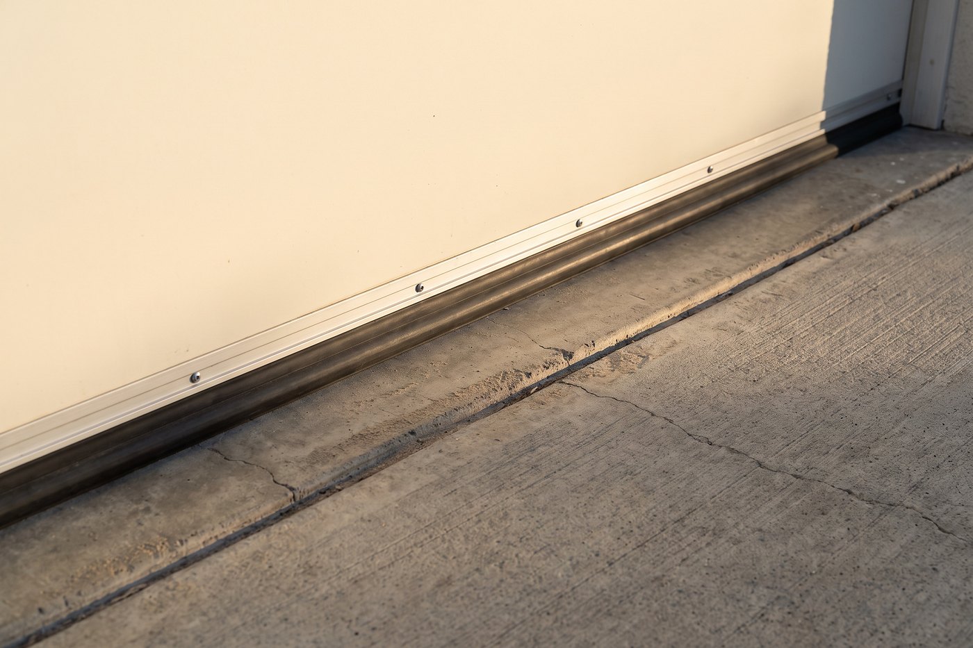 An aluminum retainer channel and rubber astragal compressed against a concrete slab in one straight line.