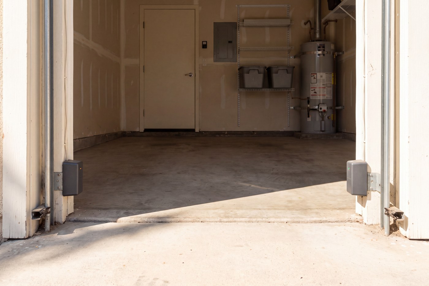A pair of safety sensors at ankle height on the two garage door tracks, one showing amber and one green.